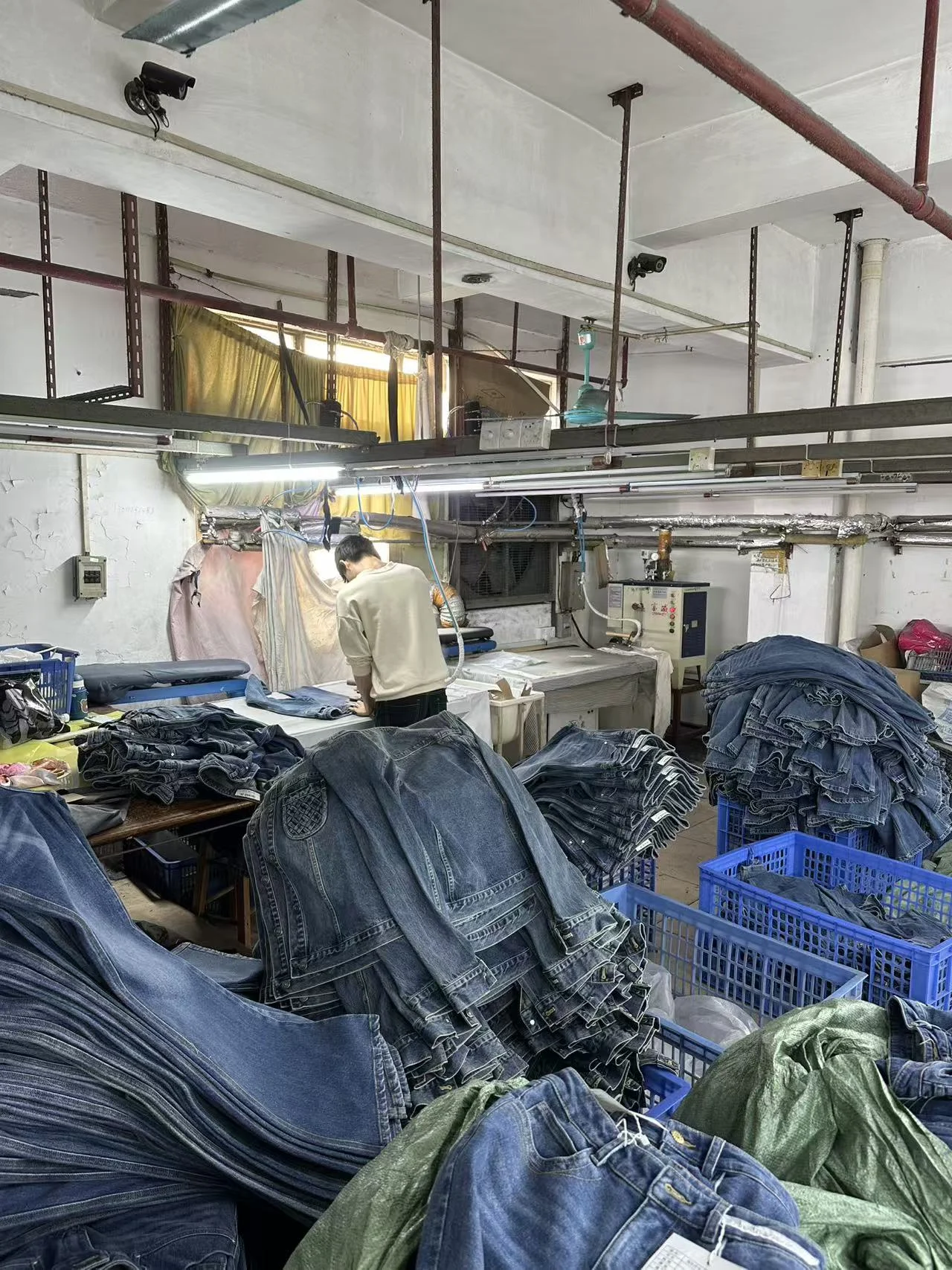A worker at the denim pressing station with folded jeans nearby