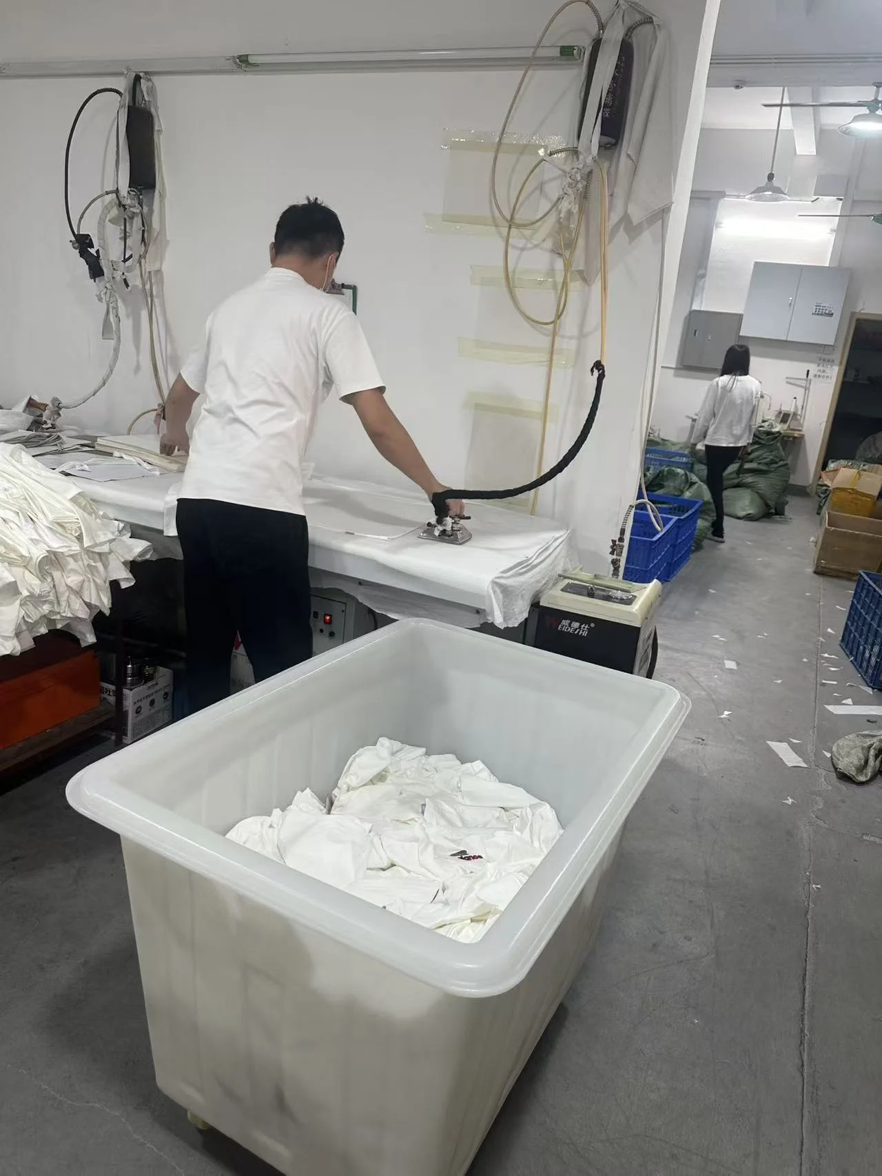 A worker pressing a light garment at a steam ironing table