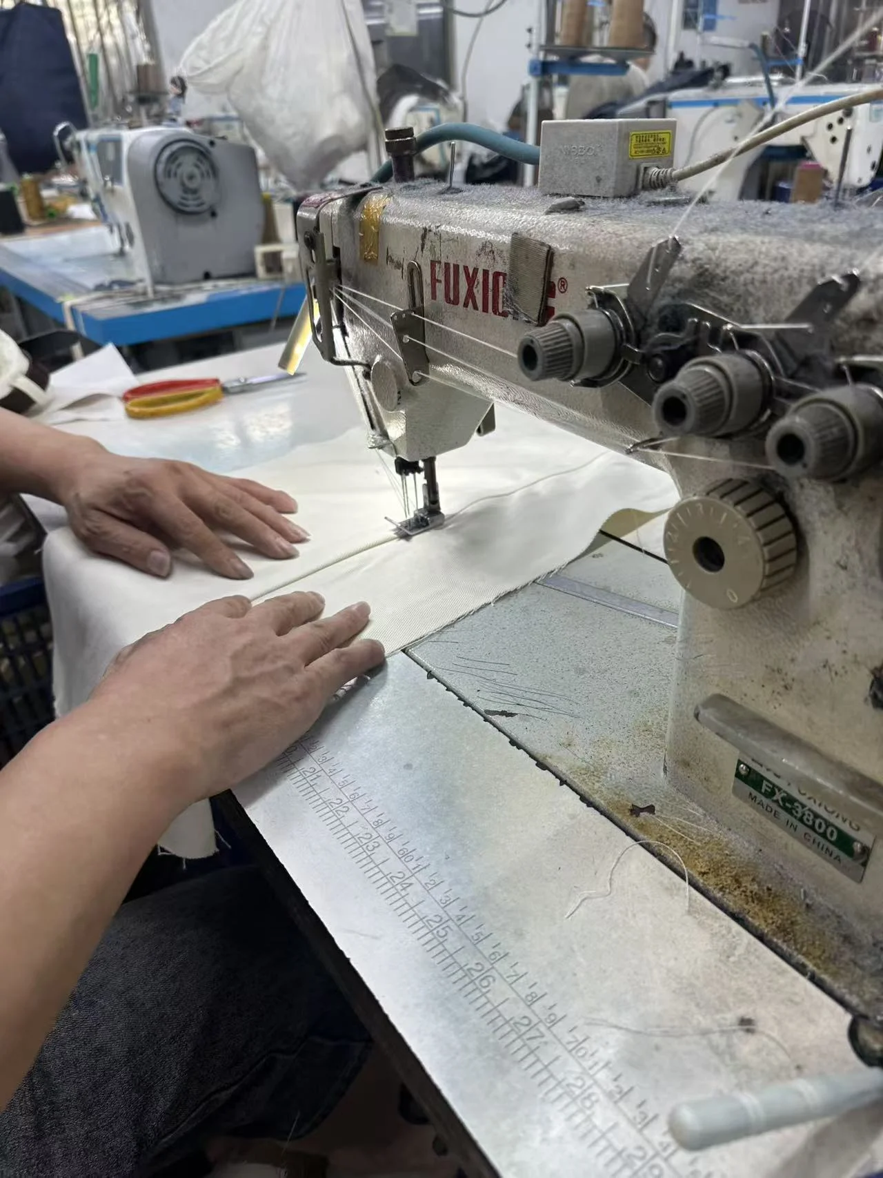 Close view of hands guiding light fabric through an industrial sewing machine